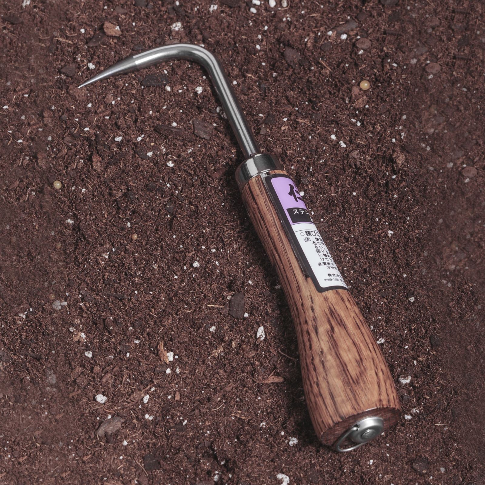 Nisaku Nekaki Ippondume Japanese Stainless Steel Single Claw Cultivator laying in soil.