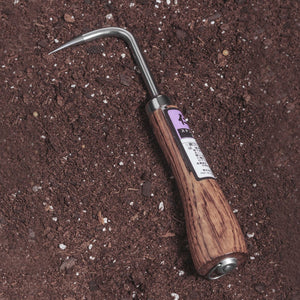Nisaku Nekaki Ippondume Japanese Stainless Steel Single Claw Cultivator laying in soil.