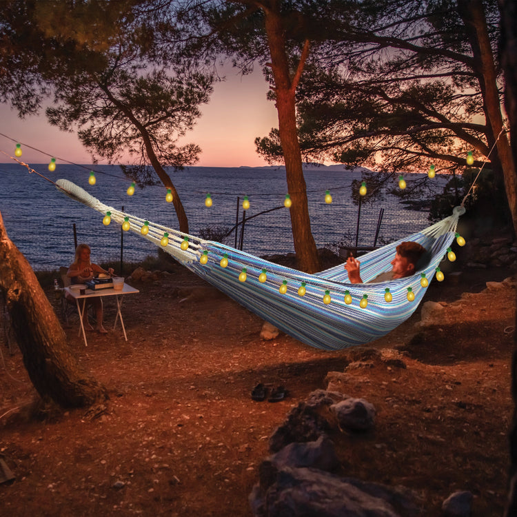 Person laying in a hammock at sunset with the strong lights hung around their hammock.