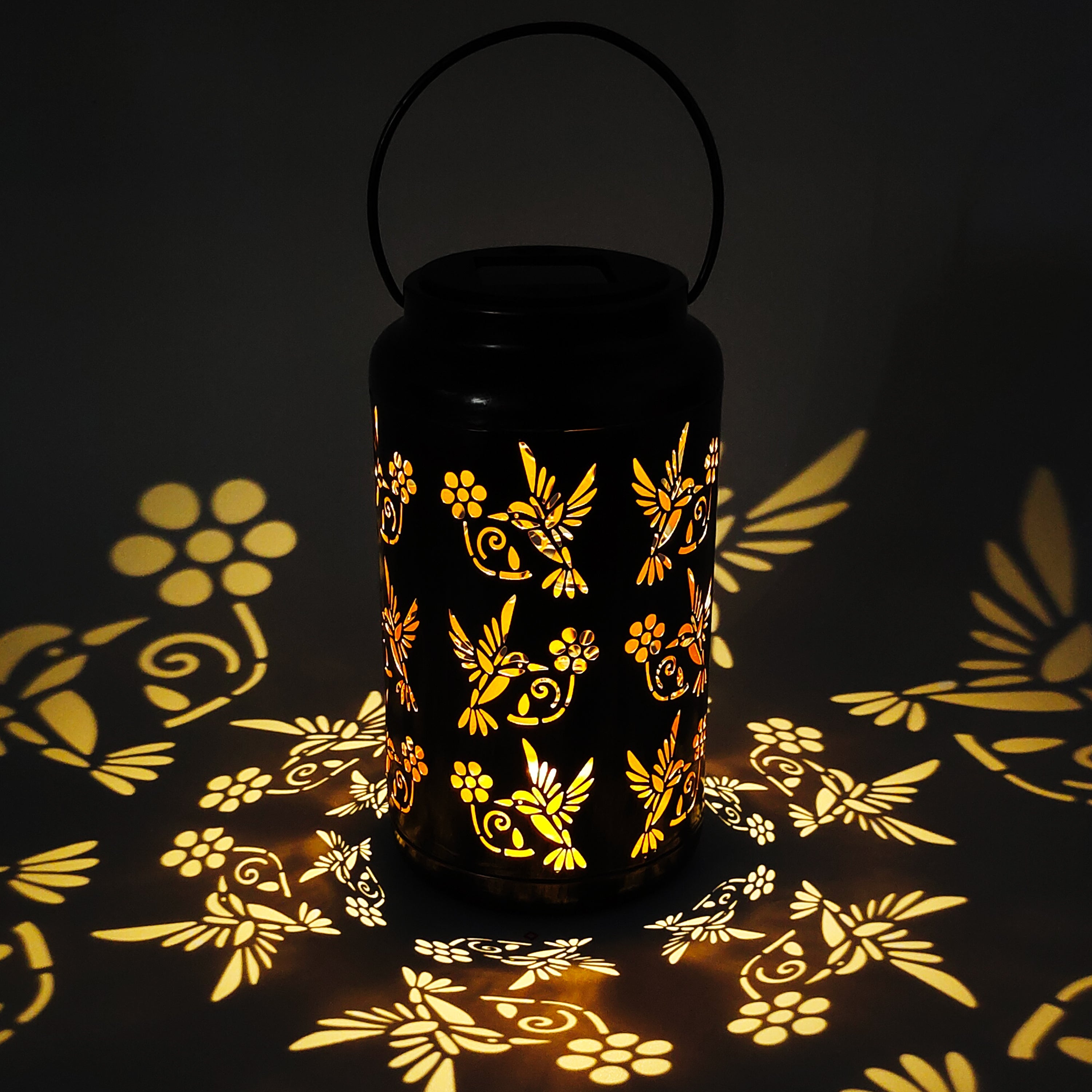 Lantern with humming bird design creating a light pattern on the surface around it.