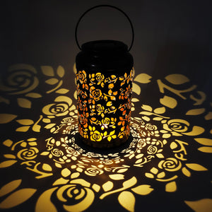 Lantern with rose design creating a light pattern on the surface around it.