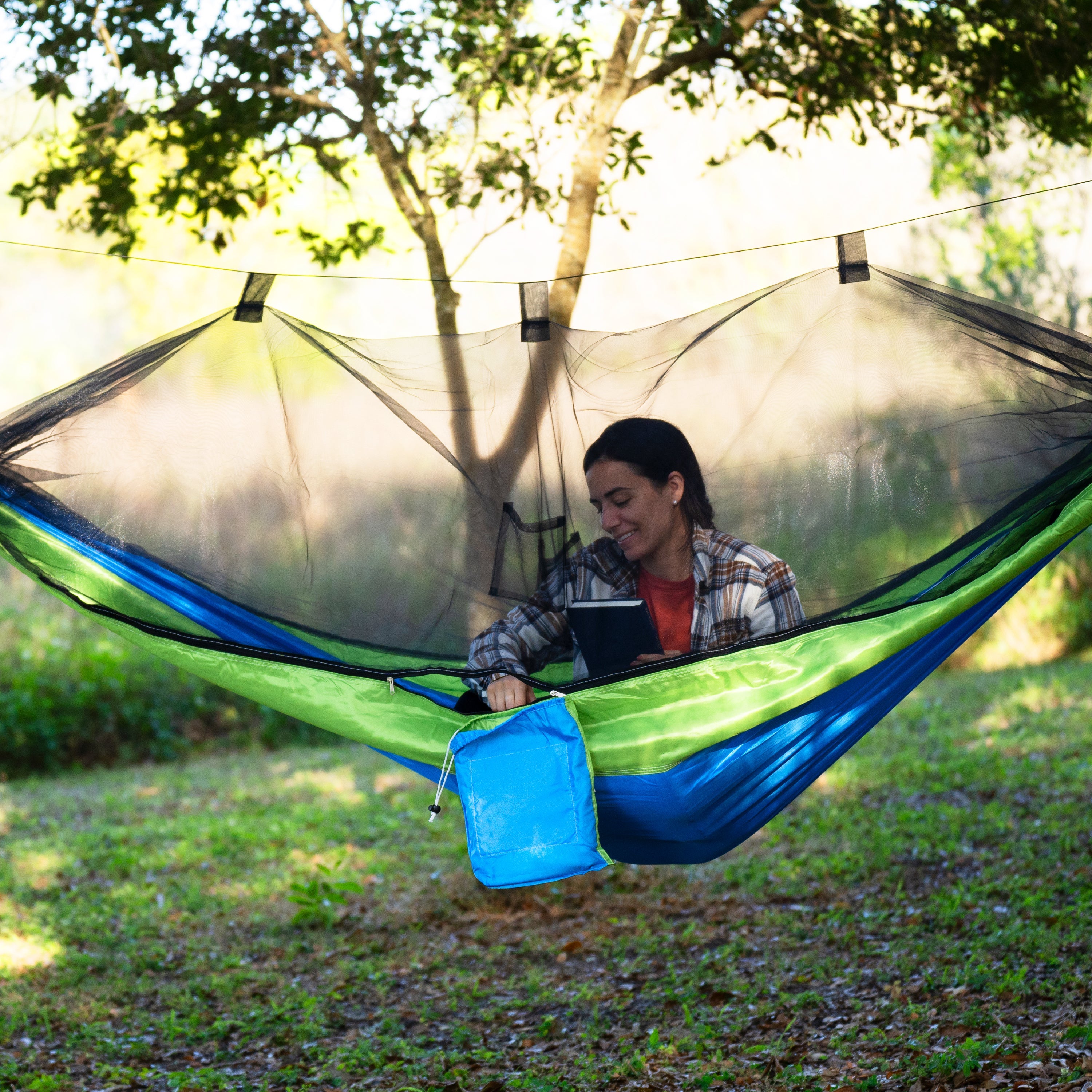 Woman sitting outside in the Bliss Hammocks 54-inch wide Mermaid-variation Camping Hammock with the mosquito net zippered shut.
