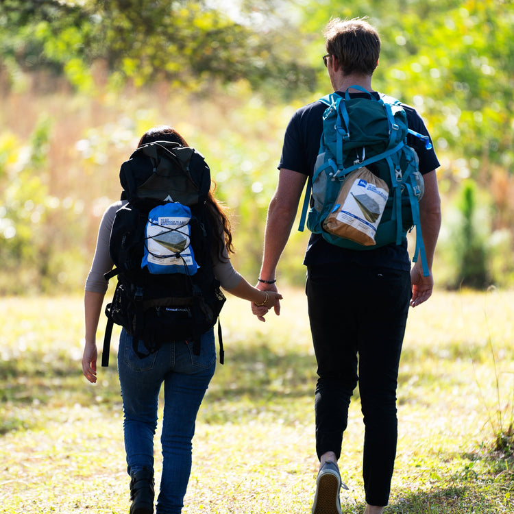 Couple holding hands with the hammock in a bag attached to their backpacks.