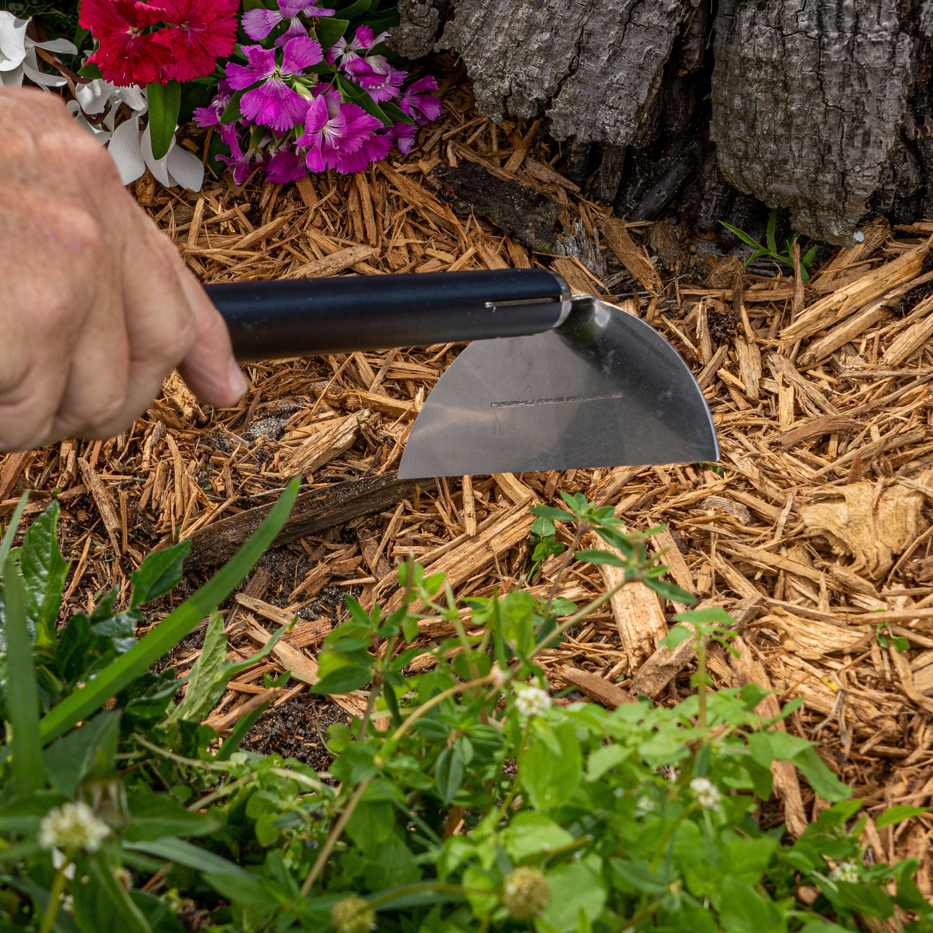 Person using the Nisaku Kusakaki 4.75-inch Japanese Stainless Steel Handheld Garden Hoe to move mulch.