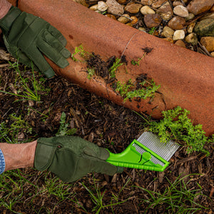 Nisaku Zassou Burush Tongari 3-inch Stainless Steel Angled Weeder being used to pull weeds from the area next to a garden.
