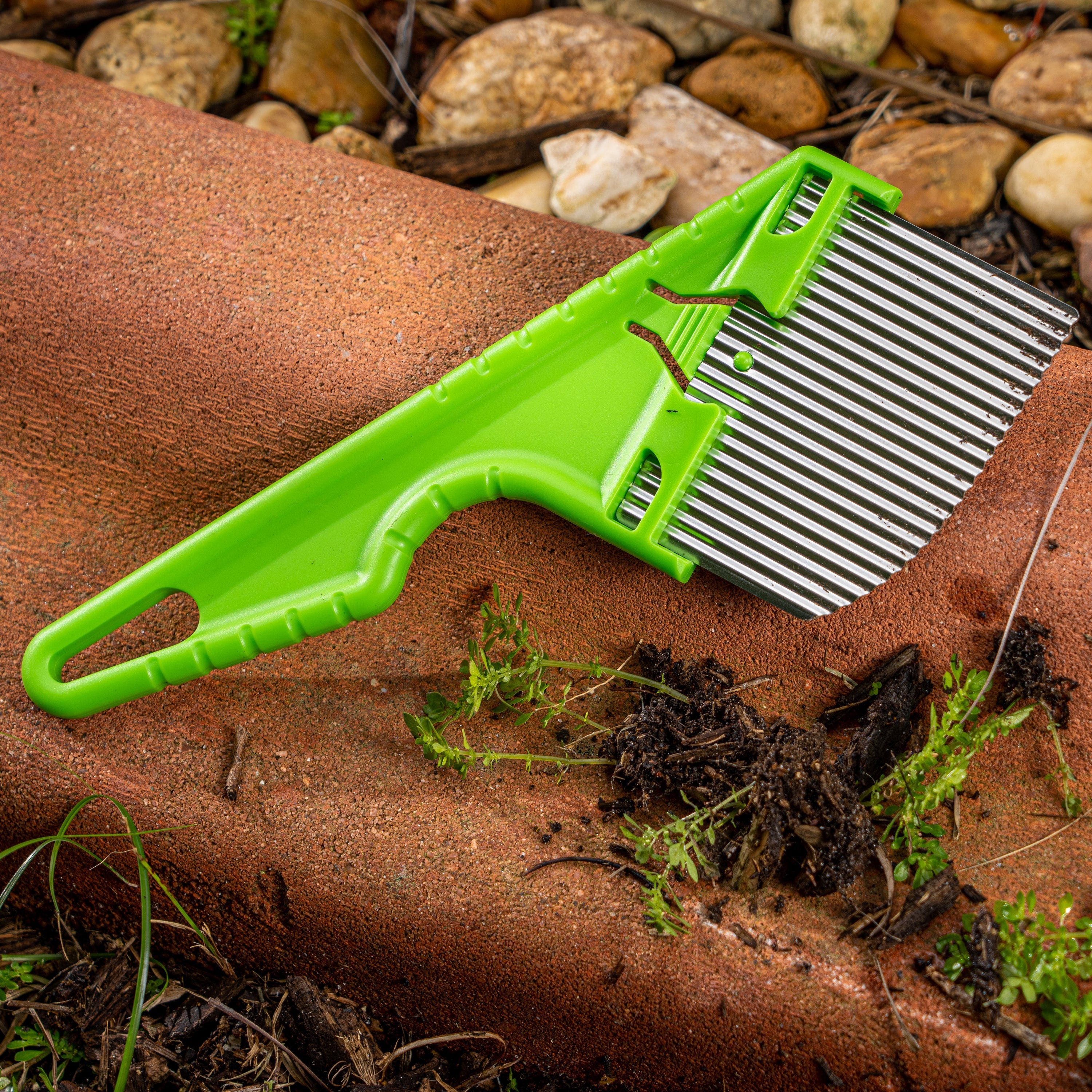 Nisaku Zassou Burush Tongari 3-inch Stainless Steel Angled Weeder outside next to rocks.