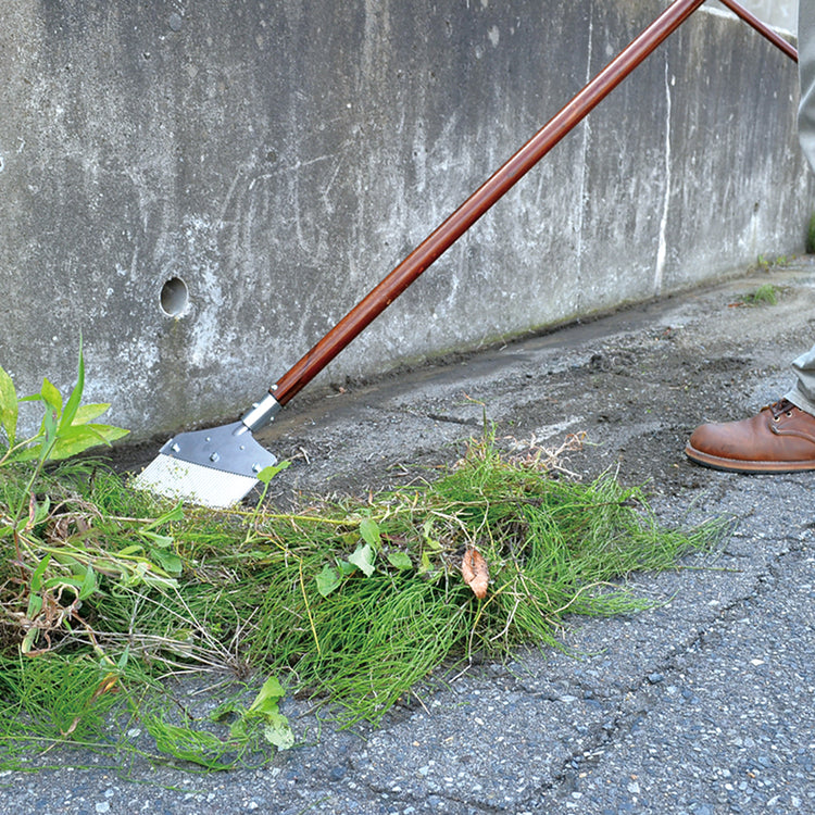 Nisaku Zassou Burush Obake 7.25-inch Stainless Steel Weed Sweeper being used to sweep weeds from a driveway.