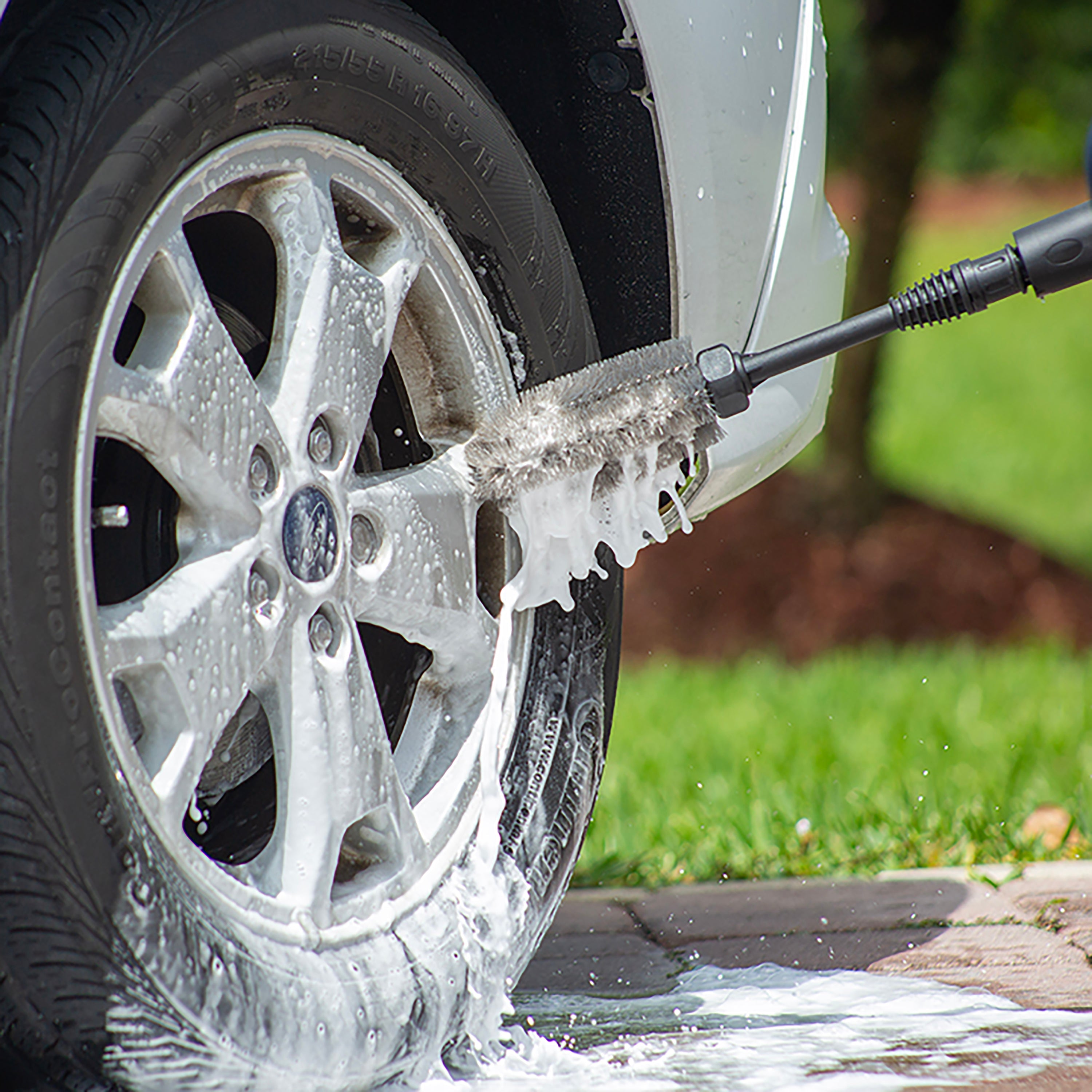 Sun Joe Universal Wheel and Rim Brush for SPX Series Pressure Washers being used to wash a tire and rim on a car.