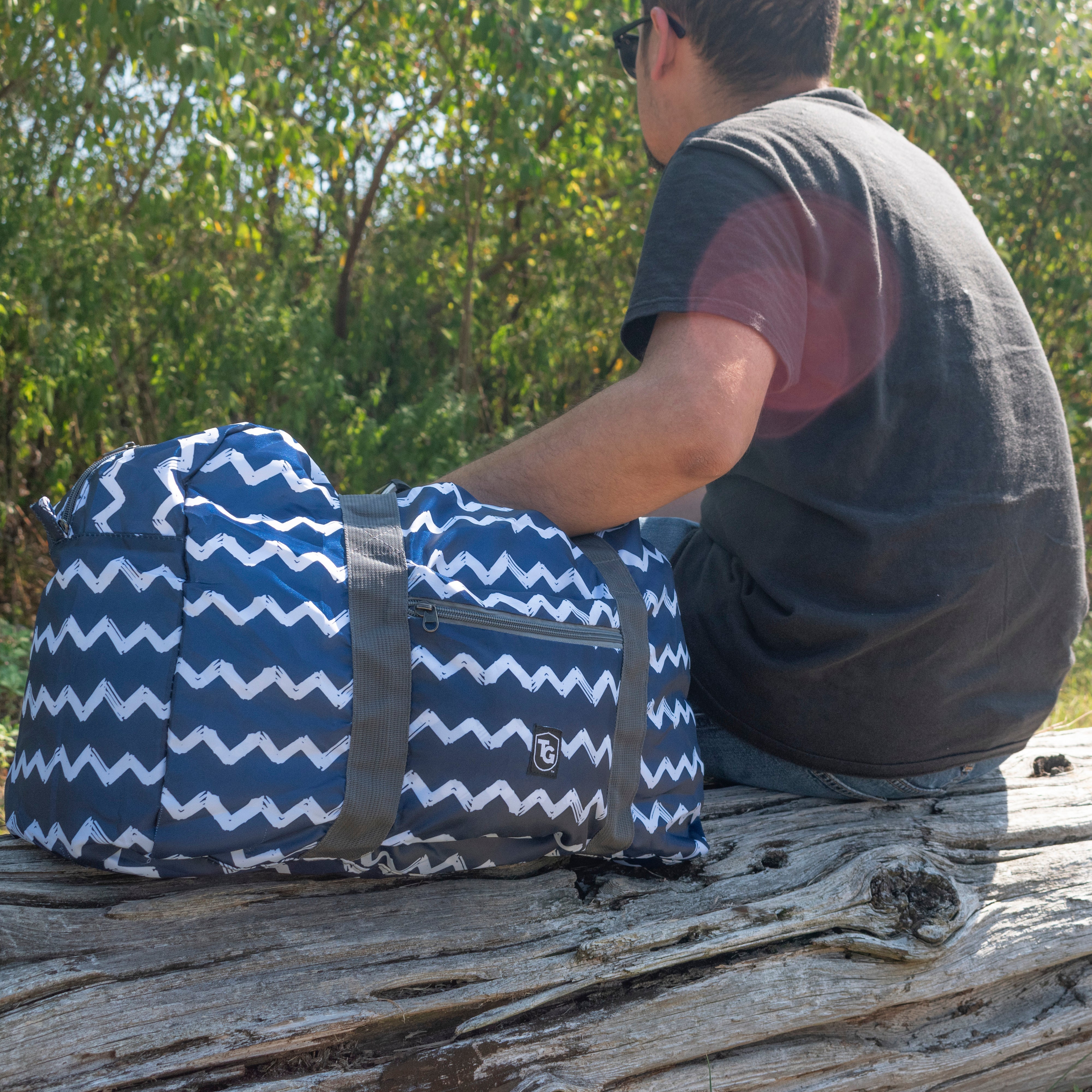 TrailGear 20-liter sky blue transparent dry bag next to a man on a log.