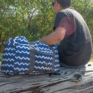 TrailGear 20-liter sky blue transparent dry bag next to a man on a log.