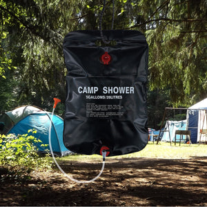 TrailGear 20-liter solar shower bag hanging from a tree with a camp in the background.