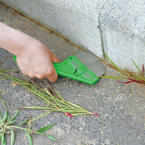 Nisaku Zassou Burush 3-inch Stainless Steel Rounded Weeder being used to get rid of weeds between the ground and a wall.